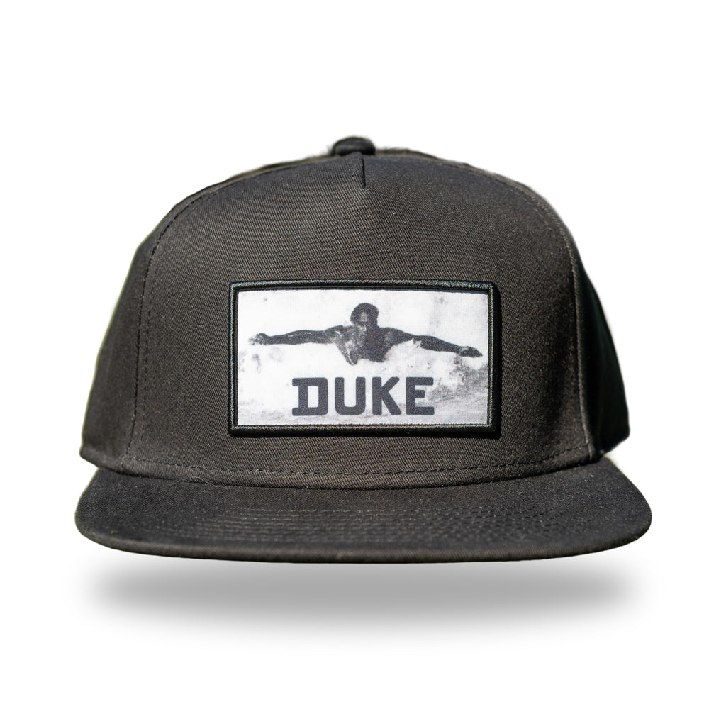 Black flat-brim snapback with woven black and white photo patch of Duke Kahanamoku swimming
