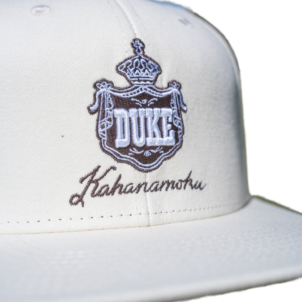 Close-up of brown DUKE royal crown crest embroidery on cream cap