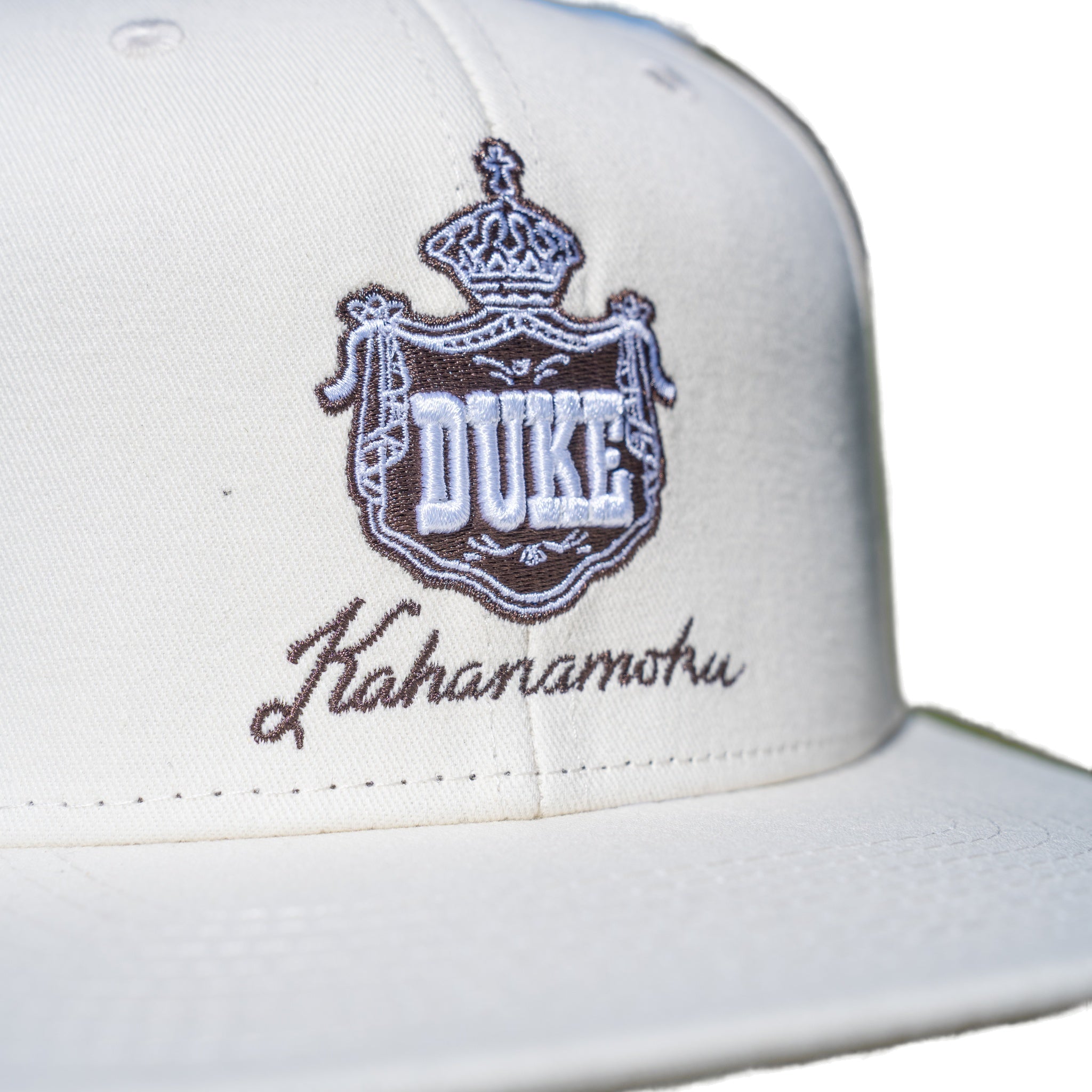 Close-up of brown DUKE royal crown crest embroidery on cream cap