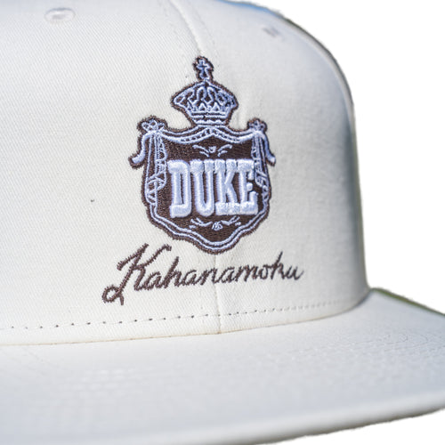 Close-up of brown DUKE royal crown crest embroidery on cream cap