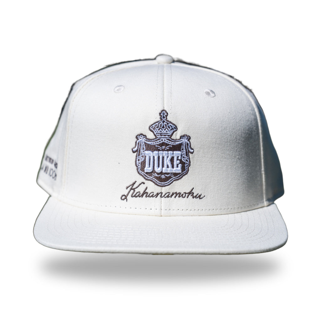 Cream snapback cap with brown embroidered Hawaiian royal crest reading DUKE and Kahanamoku script