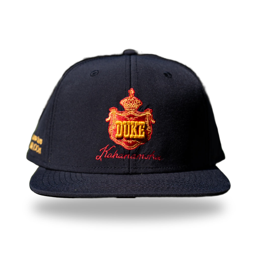Navy snapback cap with red and gold embroidered Hawaiian royal crest reading DUKE and Kahanamoku script